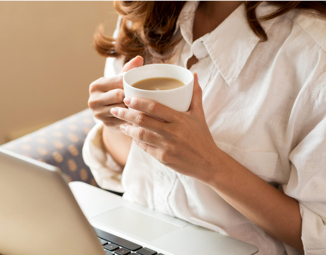 Woman holding a coffee mug while attending a telehealth therapy session on a laptop