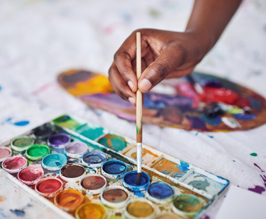 Close-up of a hand dipping a paintbrush into a watercolor palette during an art therapy session